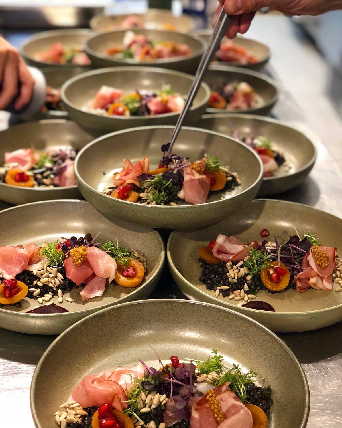 Mehrere Teller werden für das Catering präzise mit einer Pinzette angerichtet