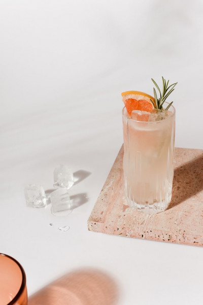 Rosaner Cocktail mit Orange & Rosmarin garniert