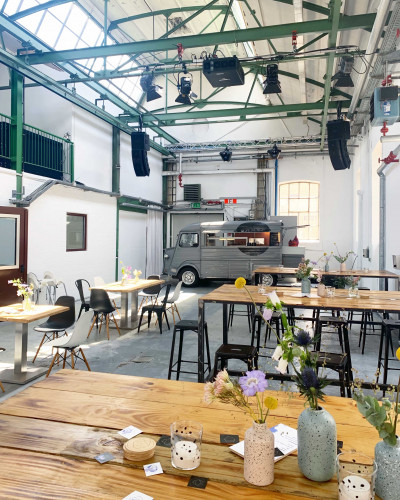 Blick in die Eventlocation, dort stehen mehrere Tische und weit hinten der Streetfood Foodtruck