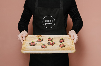 Person in a GOOSE Gourmet apron holding a finger food platter