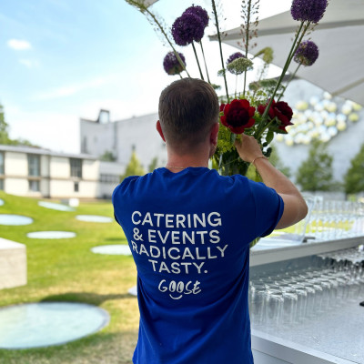 GOOSE Gourmet Mitarbeiter beim Blumen anrichten. Auf dem Shirt steht: Catering & Events Radically Tasty