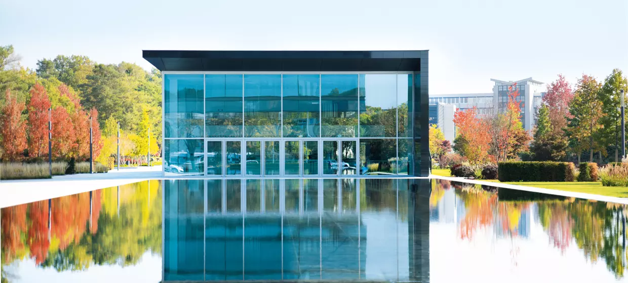 Außenfassade eines modernen Glasbaus vor einem großen Teich