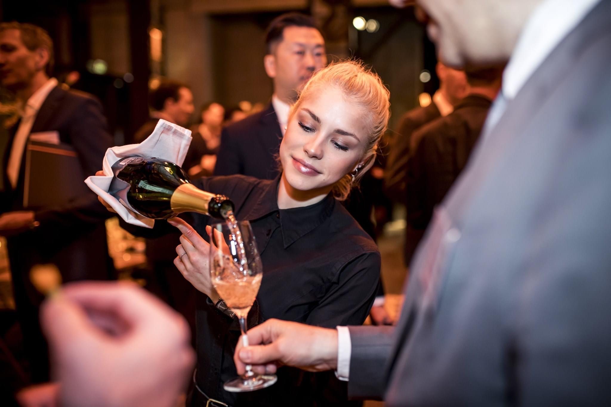 Freundliche Servicekraft beim Ausschenken von Champagner