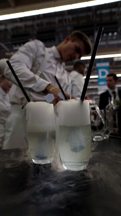 Cocktails im Vordergrund, Servicemitarbeiter beim Zubereiten der Cocktails im Hintergrund